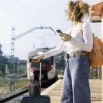 Mujer esperando tren con maleta de viaje, llevando bolsa compacta con Ergo Travel Pillow, lista para usar en trayecto largo